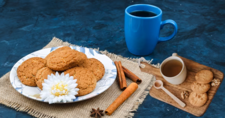 Coconut Cookies Recipe: घर पर नारियल से बनाएं बाजार जैसी कुरकुरी कुकीज Fresh homemade coconut cookies served on a wooden plate with grated coconut and a cup of tea.